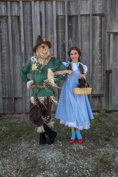 two people dressed up as scarecrows and one is holding a basket full of hay