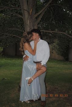 a man and woman kissing in front of a tree at night with their arms around each other