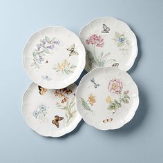 four plates with flowers and butterflies painted on them, all in different shapes and sizes