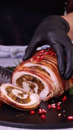 a person in black gloves is slicing meat on a plate with pomegranates