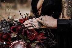 a tattooed woman holding a bouquet of red flowers and greenery with her hands resting on the man's arm