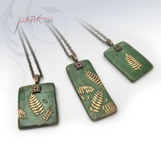 three green and gold necklaces with fern leaves on the front, two are hanging from chains