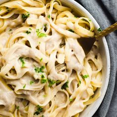 a white bowl filled with pasta covered in sauce and parsley