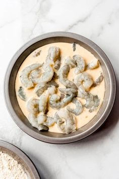 a bowl filled with batter and shrimp on top of a white countertop next to two bowls