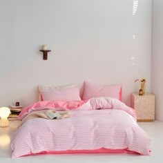 a bed with pink sheets and pillows in a white room next to a night stand