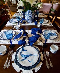 the table is set with blue and white plates, silverware, and vases