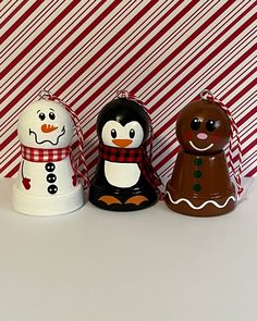 three ceramic snowmen are standing next to each other on a white surface with red and white striped background