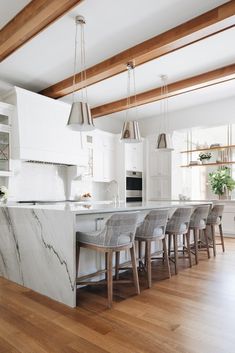 a kitchen with white cabinets and marble counter tops, wooden floors, and hanging lights