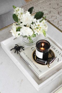 a candle and some white flowers on a tray with a book in the corner next to it