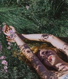 a woman laying in the grass with her hands on her head and flowers around her body