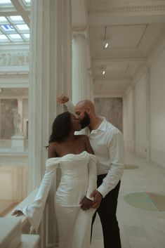 a man and woman are kissing in an art gallery, with columns on either side