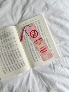 an open book laying on top of a bed next to a pink ribbon and pen