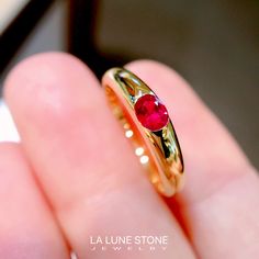 a close up of a person's hand holding a gold ring with a red stone