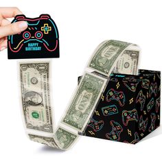 a hand holding a video game controller and money in front of a black gift box