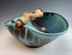 a ceramic bowl with a wooden stick sticking out of it's side, on a white surface