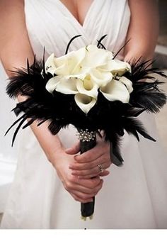 a woman in a white dress holding a black and white bridal bouquet with feathers