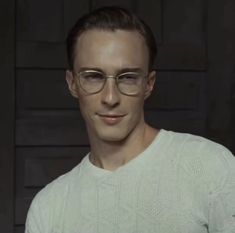 a man wearing glasses standing in front of a black background