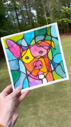 a hand holding up a card with a colorful dog on it's face in the grass