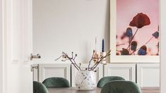 a dining room table with green chairs and a vase filled with flowers on top of it