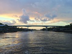 the sun is setting and there are boats on the water in front of an overpass