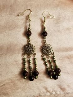 These unique earrings are handmade, a chandelier style that dangles 4 inches from the ear. Carefully beaded with a combination of glass, ceramic, and metal. Bohemian Beaded Chandelier Earrings With Czech Glass, Bronze Dangle Chandelier Earrings, Bronze Beaded Dangle Earrings, Handmade Bronze Dangle Chandelier Earrings, Handmade Czech Glass Chandelier Earrings, Beaded Czech Glass Chandelier Drop Earrings, Brown Czech Glass Earrings With Dangling Beads, Brown Dangle Chandelier Earrings With Beads, Golden Chandelier