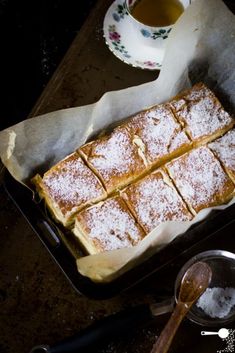 powdered sugar covered pastry sitting on top of a pan next to a cup of tea