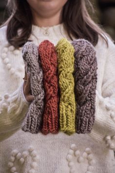 a woman holding three knitted mittens in her hands