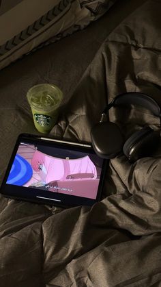 an ipad with headphones and a cup of green tea on a bed next to it