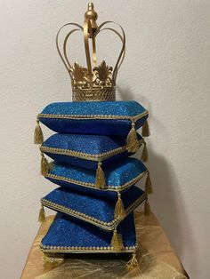 a stack of blue pillows with a gold crown on top is sitting on a table