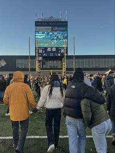 people are walking on the field in front of a large scoreboard at a football game