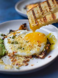 an egg is being drizzled over some toast with avocado on the side