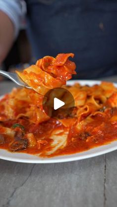 a person is holding a fork over a plate of pasta with sauce and meat on it