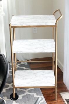 three tiered white marble and gold metal serving cart in the corner of a living room