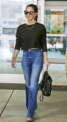 a woman in black shirt and jeans walking down the street with her hand on her hip