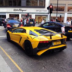 a yellow sports car is parked on the side of the road in front of some cars