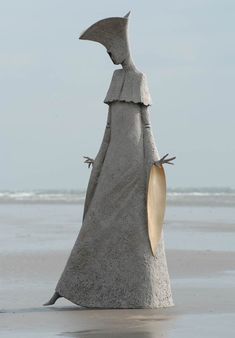 a statue is standing on the beach and has a surfboard in it's hand