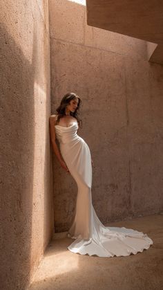 a woman in a white dress leaning against a wall