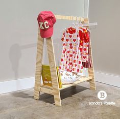 a child's bed with a hat on top and clothes hanging from the rails