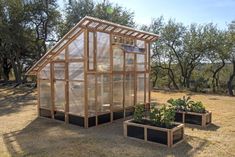 two small greenhouses with plants in them on the ground near some trees and grass