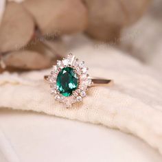 an emerald colored stone surrounded by small white diamonds on top of a piece of cloth