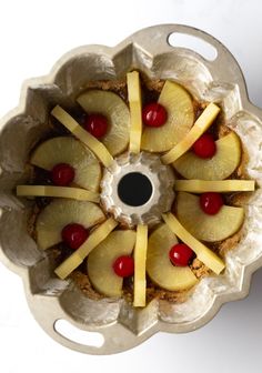 pineapple and cherries are arranged in the center of a cake dish on a white surface