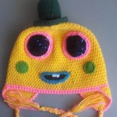 a crocheted yellow hat with eyes and a green cap on it's head