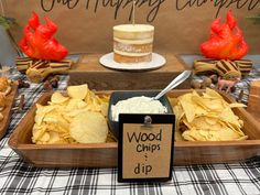 a wooden tray filled with chips next to a cake on top of a tablecloth