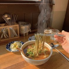 someone is holding chopsticks over a bowl of soup with noodles and vegetables in it