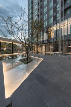 an empty courtyard in front of a tall building with trees on the ground and water reflecting off it's sides