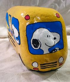 a yellow and blue painted rock shaped like a bus with snoopy on the front