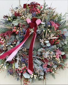 a christmas wreath hanging on the side of a white door with red ribbon and berries