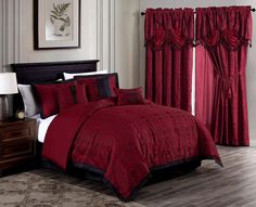 a bed with red and black comforters in a bedroom next to a window filled with curtains