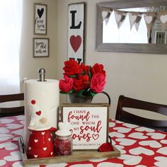 a table topped with red roses next to a sign and vase filled with pink flowers