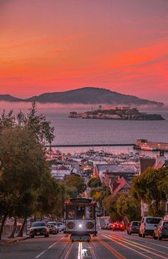 a trolley car traveling down a street next to the ocean at sunset in san francisco, california